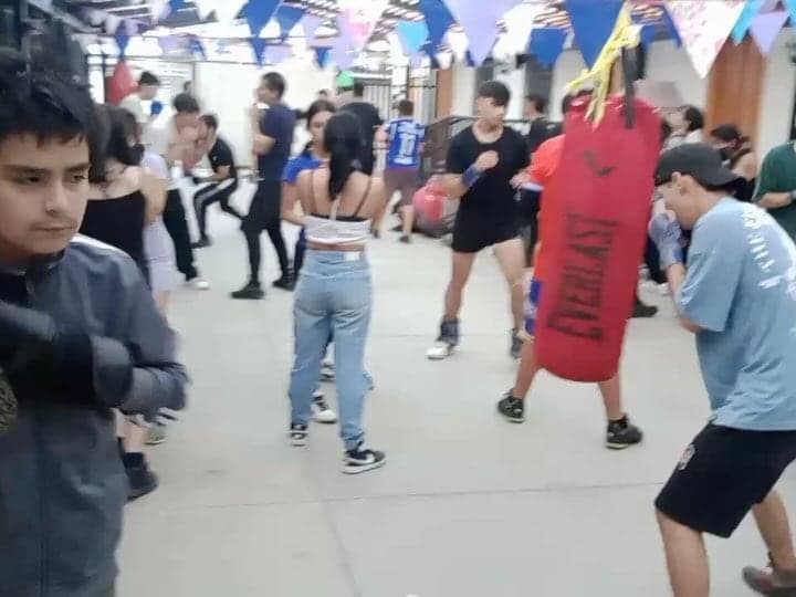 Jóvenes golpeando sacos en un patio techado con banderines