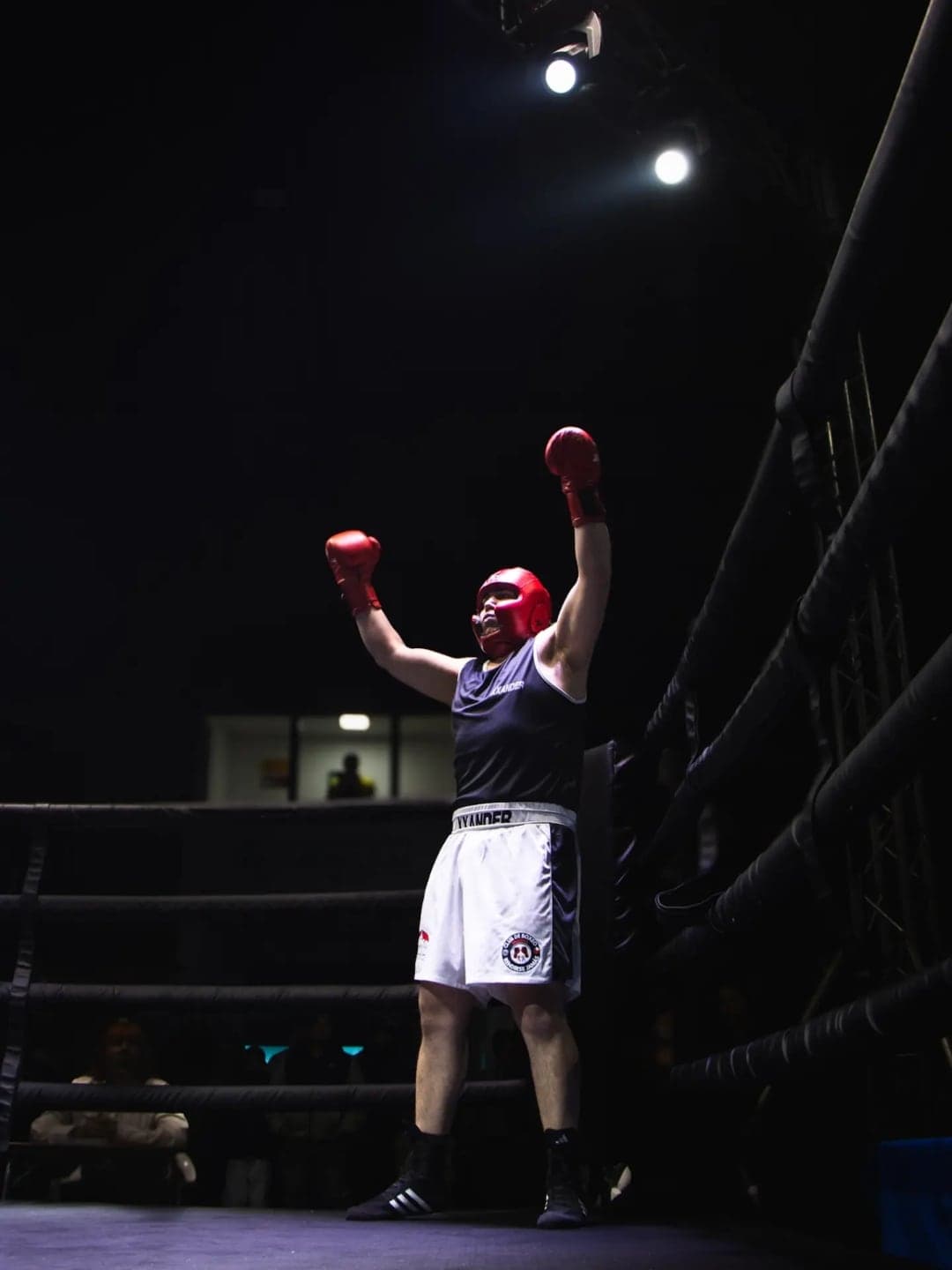 Boxeador del club con los brazos en alto bajo los focos del ring, en la velada de Molina