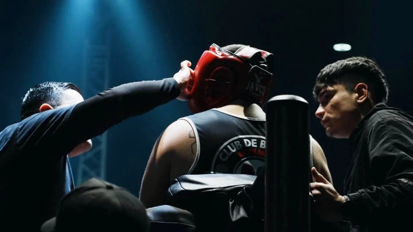 En la esquina del ring, el entrenador acomoda el cabezal de un boxeador del club entre rounds